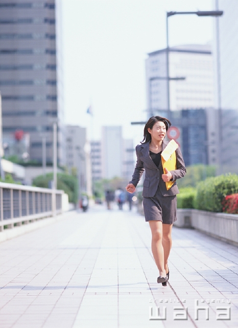 イラスト＆写真のストックフォトwaha（ワーハ）　人物、日本人、ビジネス、ビジネスウーマン、女性、走る、屋外、正面、全身、営業、ビジネス街、ビル街、街角、都会的、ストリート、空、書類、封筒、街並み、街並、仕事、働く、OL　p2-1511b