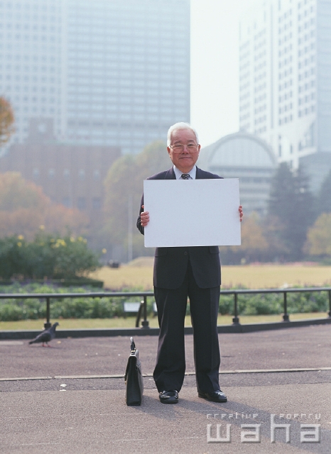 イラスト＆写真のストックフォトwaha（ワーハ）　人物、日本人、メッセージボード、ビジネス、ビジネスマン、男性、シニア、屋外、正面、全身、ポートレート、ビル街、都会的、通勤、営業、カバン、メガネ、真面目、街並み、街並、仕事、働く、サラリーマン　p2-2072a