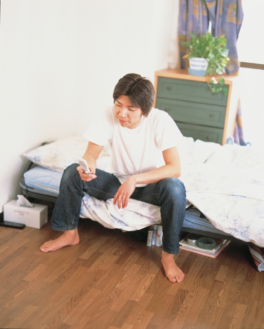 イラスト＆写真のストックフォトwaha（ワーハ）　人物、日本人、若者、10代、20代、男性、1人、屋内、部屋、ベット、携帯電話、若者1人暮らし、全身　p3-1324b
