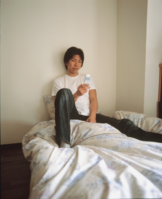 イラスト＆写真のストックフォトwaha（ワーハ）　人物、日本人、若者、10代、20代、男性、1人、屋内、部屋、ベット、携帯電話、若者1人暮らし、全身　p3-1329b
