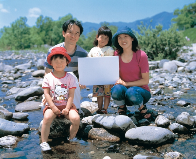 イラスト＆写真のストックフォトwaha（ワーハ）　人物、日本人、家族、親子、4人、父、母、娘、屋外、川、座る、メッセージボード、正面、全身、水　p3-1369b