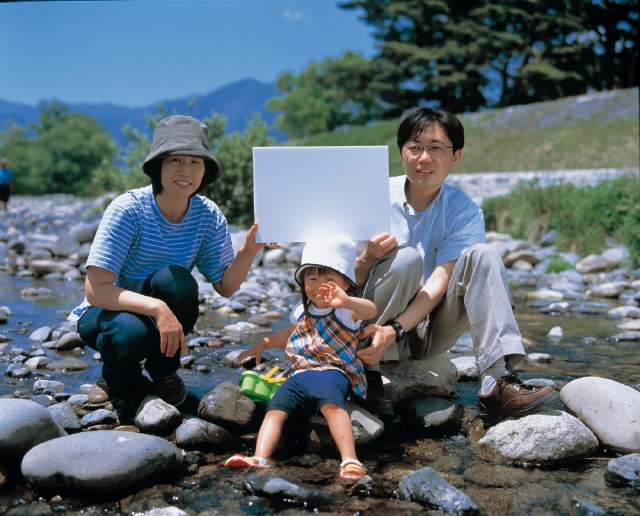 イラスト＆写真のストックフォトwaha（ワーハ）　人物、日本人、家族、親子、3人、父、母、娘、屋外、川、座る、メッセージボード、正面、全身、水　p3-1370b