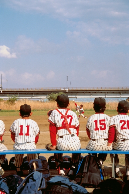 イラスト＆写真のストックフォトwaha（ワーハ）　人物、日本人、小学生、学生、スポーツ、屋外、グループ、集合、仲間、チームメイト、後ろ姿、全身、クラブ活動、野球、ユニフォーム、キャップ帽子、応援、グラウンド、試合、見守る、青空、ベンチ、座る、後姿、後ろ姿、うしろ姿、背中、運動、エール　p4-1070b