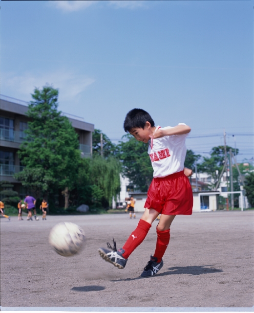 イラスト＆写真のストックフォトwaha（ワーハ）　人物、日本人、小学生、学生、スポーツ、子供、屋外、横向き、横顔、全身、ブレ、サッカーボール、ユニフォーム、キック、蹴る、青空、グラウンド、校庭、躍動感、運動、子ども、こども　p5-0110b