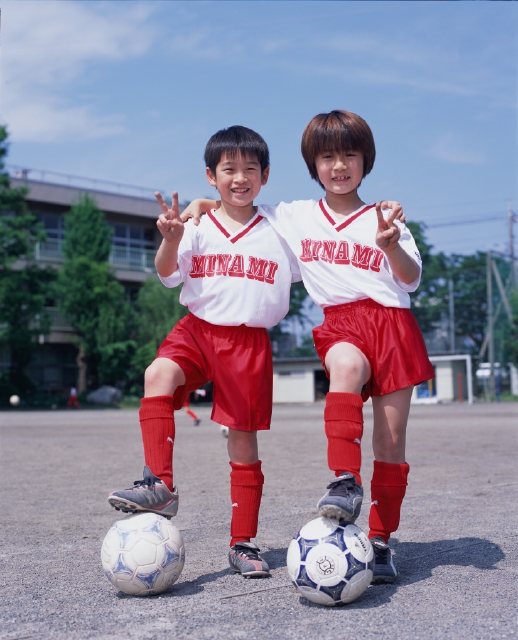 イラスト＆写真のストックフォトwaha（ワーハ）　人物、日本人、小学生、学生、子供、スポーツ、屋外、正面、全身、ポートレート、ポーズ、Vサイン、2人、サッカーボール、ユニフォーム、青空、グラウンド、校庭、片足をのせる、きめる、格好をつける、友達、グループ、仲間、チームメイト、運動、子ども、こども　p5-0112b