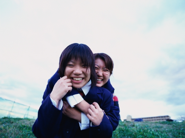イラスト＆写真のストックフォトwaha（ワーハ）　人物、日本人、若者、笑顔、元気、健康、高校生、学生、屋外、正面、上半身、ポートレート、2人、友達、抱きつく、抱く、ふざける、はしゃぐ、土手、笑う、笑い、スマイル、女子高生　p5-0553b