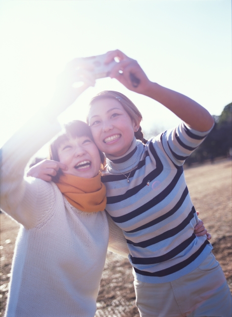 イラスト＆写真のストックフォトwaha（ワーハ）　人物、日本人、若者、公園、屋外、正面、上半身、逆光、2人、女の子、女性、カメラ、写真、チーズ、ポーズ、広場、草原、笑う、嬉しい、楽しい、はしゃぐ、マフラー、笑う、笑い、スマイル　p6-0941b