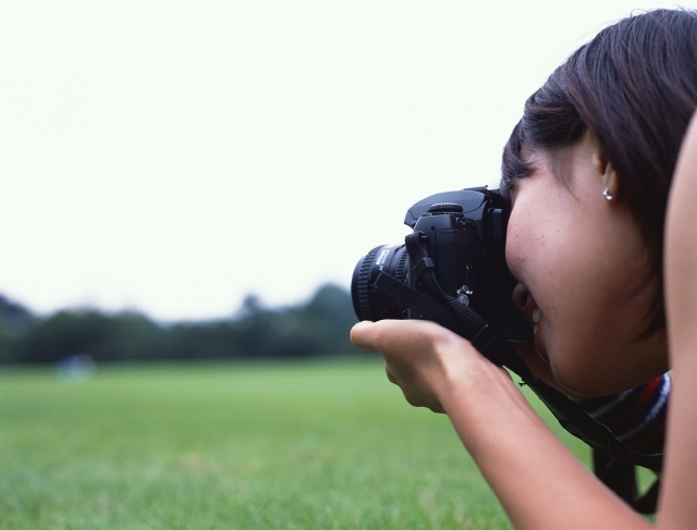 イラスト＆写真のストックフォトwaha（ワーハ）　人物、日本人、若者、公園、屋外、横向き、横顔、上半身、女の子、女性、カメラ、レンズ、写真、チーズ、広場、草原、覗く、趣味、好奇心　p6-0952bv