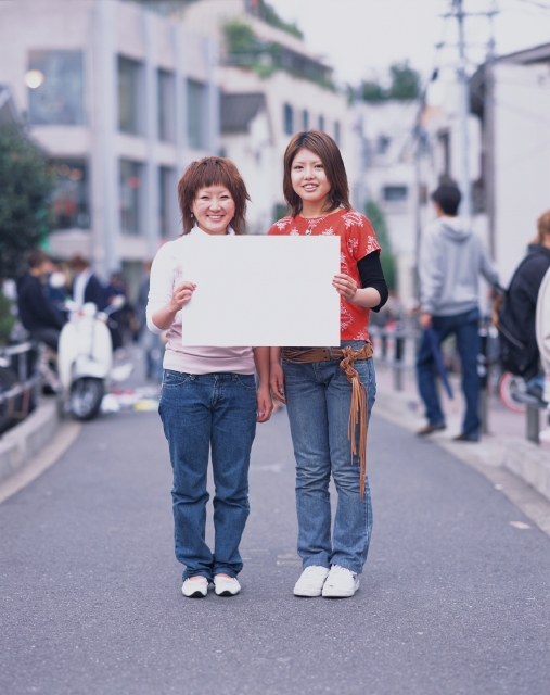 イラスト＆写真のストックフォトwaha（ワーハ）　人物、日本人、メッセージボード、若者、屋外、正面、全身、ポートレート、2人、女の子、女性、嬉しい、ジーンズ、街角、ストリート、街並み、街並　p6-1868b