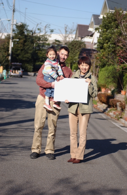 イラスト＆写真のストックフォトwaha（ワーハ）　人物、日本人、メッセージボード、家族、屋外、正面、全身、ポートレート、3人、父、母、子供、娘、愛情、親子、女の子、幼い、無邪気、元気、成長、幼児、住宅街、抱く、幸福感、住宅、家、子ども、こども　p8-0049b-data