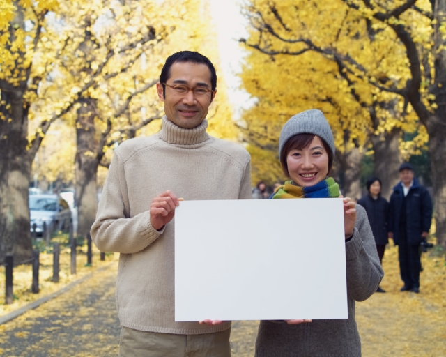 イラスト＆写真のストックフォトwaha（ワーハ）　人物、日本人、メッセージボード、公園、秋、夫婦、屋外、正面、上半身、ポートレート、2人、愛情、カップル、パートナー、夫婦、笑う、散歩、マフラー、メガネ、落ち葉、笑う、笑い、スマイル、季節、四季　p8-0140bv-data