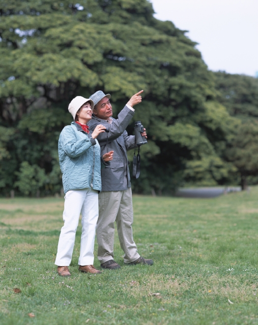 イラスト＆写真のストックフォトwaha（ワーハ）　人物、日本人、公園、レジャー、夫婦、中高年、屋外、横向き、横顔、全身、2人、男性、女性、散歩、バードウォッチング、双眼鏡、覗く、観察、調べる、発見、好奇心、指差し、広場、森林、草原　p8-1399b