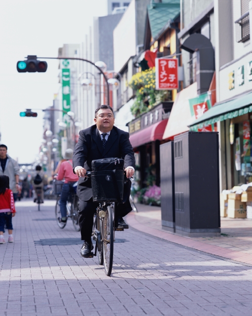 イラスト＆写真のストックフォトwaha（ワーハ）　人物、日本人、ビジネス、ビジネスマン、男性、屋外、正面、全身、真面目、通勤、営業、自転車、乗り物、街角、町角、ストリート、商店街、出発、町並、町並み、仕事、働く、サラリーマン　p9-0718b