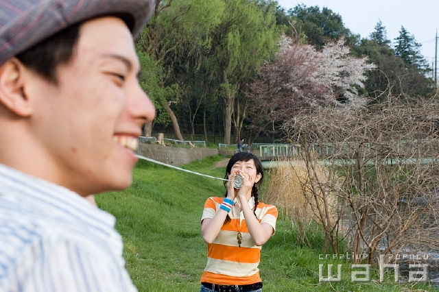 イラスト＆写真のストックフォトwaha（ワーハ）　人物、日本人、若者、コミュニケーション、カップル、正面、横向き、横顔、上半身、糸電話、草原、土手、遊ぶ、話す、聞く、あそぶ、あそび、遊ぶ、遊び　t8yg-0172b