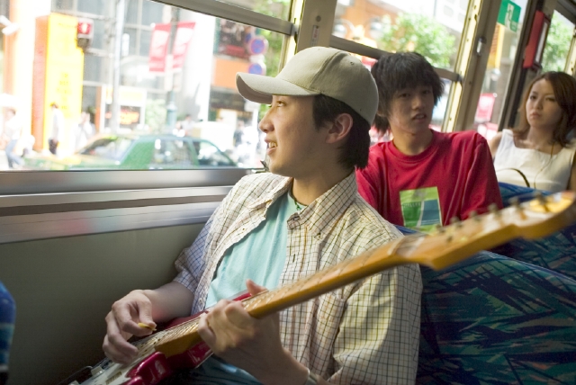 イラスト＆写真のストックフォトwaha（ワーハ）　人物、日本人、男性、若者、10代、20代、1人、屋外、車内、バス、趣味、楽器、ギター、音楽、上半身、街、街並、街並み、車内、バス　w1-7282bv