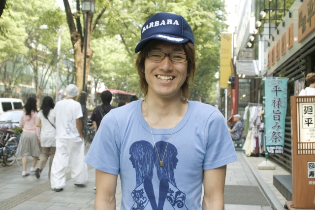 イラスト＆写真のストックフォトwaha（ワーハ）　人物、日本人、男性、若者、20代、1人、屋外、街、帽子、メガネ、笑顔、上半身、正面、ポートレート、街、街並み、街並、笑顔、笑い、笑う、スマイル　w2-2013b