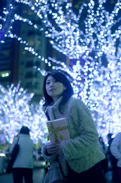 イラスト＆写真のストックフォトwaha（ワーハ）　人物、日本人、女性、20代、1人、屋外、冬、クリスマス、夜、イルミネーション、プレゼント、上半身、ギフト、贈り物、夜景、季節、四季、行事　w2-5046b