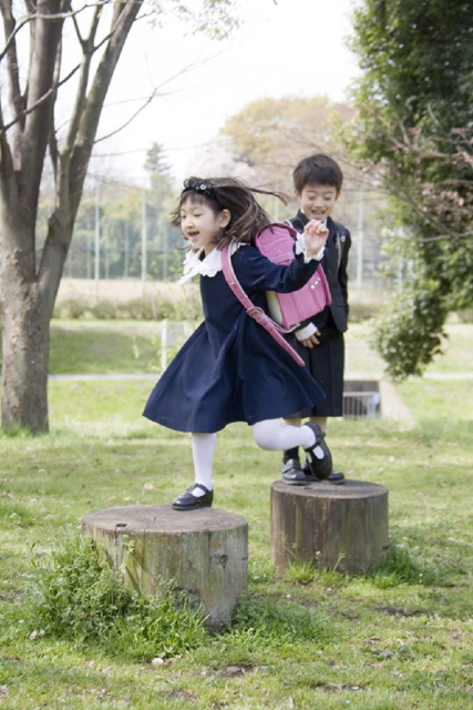 イラスト＆写真のストックフォトwaha（ワーハ）　人物、日本人、学生、小学生、男の子、女の子、2人、友達、屋外、公園、春、入学、通学、ジャンプ、遊ぶ、木、全身、あそぶ、あそび、遊ぶ、遊び、とぶ、はねる、子供、子ども、こども、季節、四季　w2-7216b